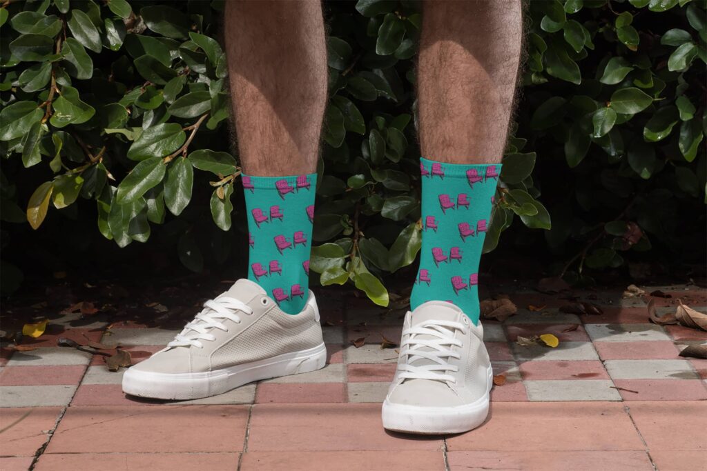 Custom merch for Front Porch Improv by Olive Ridley Studios: Teal socks printed with a repeating patterns of pink chairs