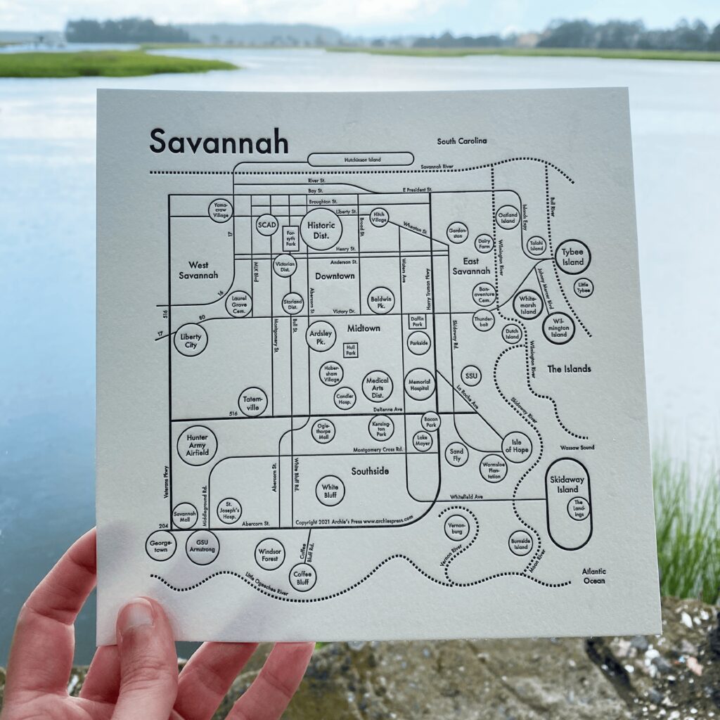 Map of Savannah created through a collaboration between Olive Ridley Studios and Archie's Press: Letterpress-printed map being held in front of a marsh view